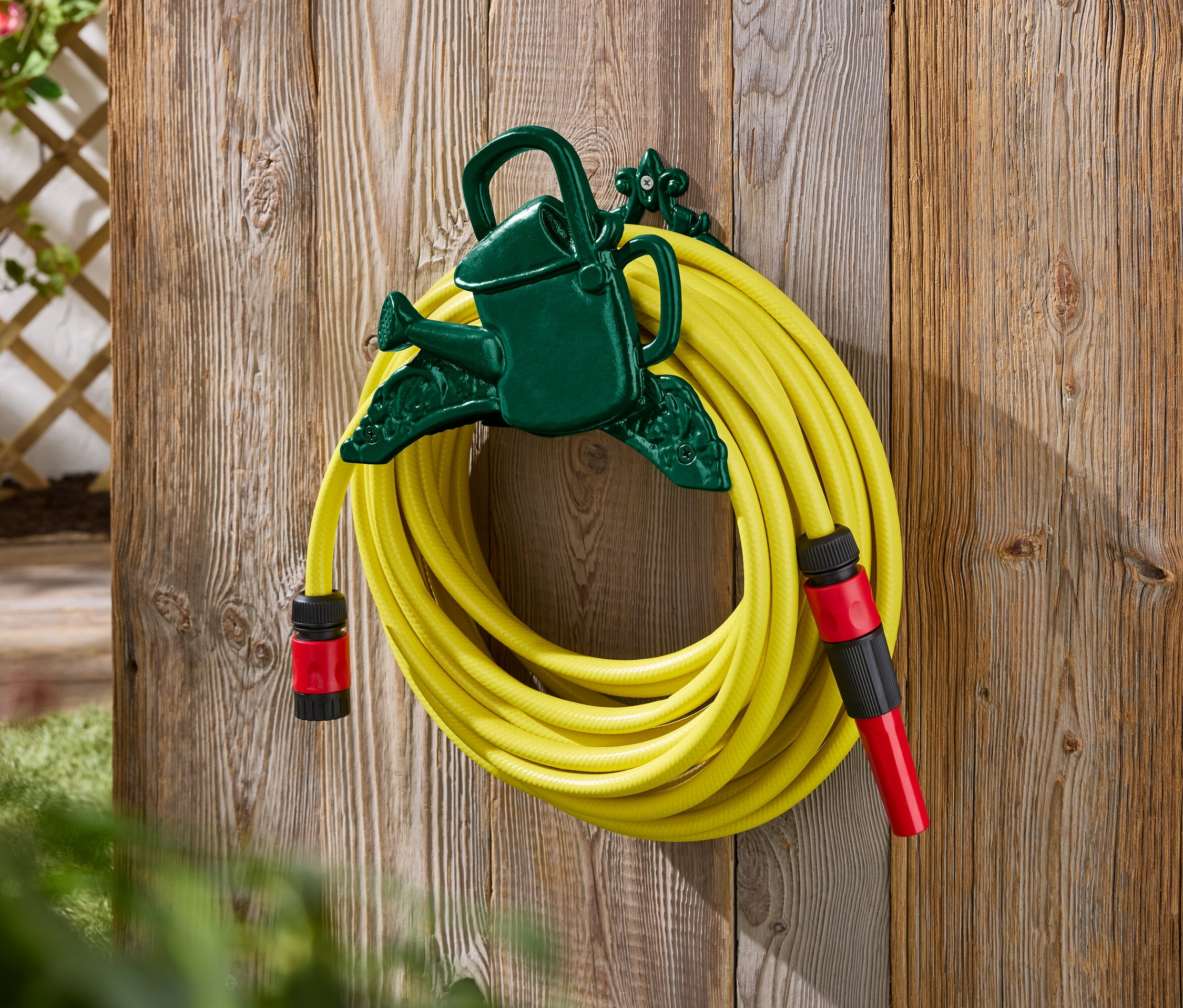 Un tuyau d'arrosage jaune est fixé à un support vert en forme d'arrosoir sur un mur en bois.
