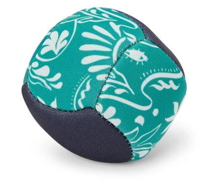 Une balle de jonglage turquoise et bleue avec un motif blanc repose sur le sol.