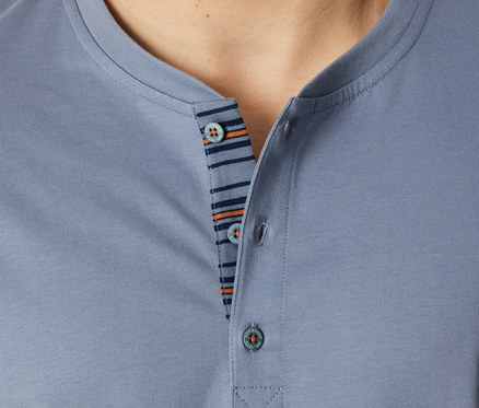 Gros plan d'une personne portant un haut de set shorty SCHIESSER bleu-gris, montrant l'encolure Henley à trois boutons et une patte de boutonnage rayée bleu foncé et orange.