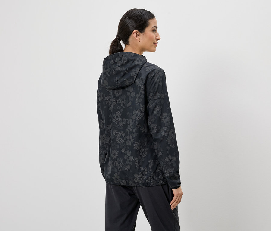 Femme vue de dos portant une veste et un pantalon noirs à motifs floraux sur fond clair.