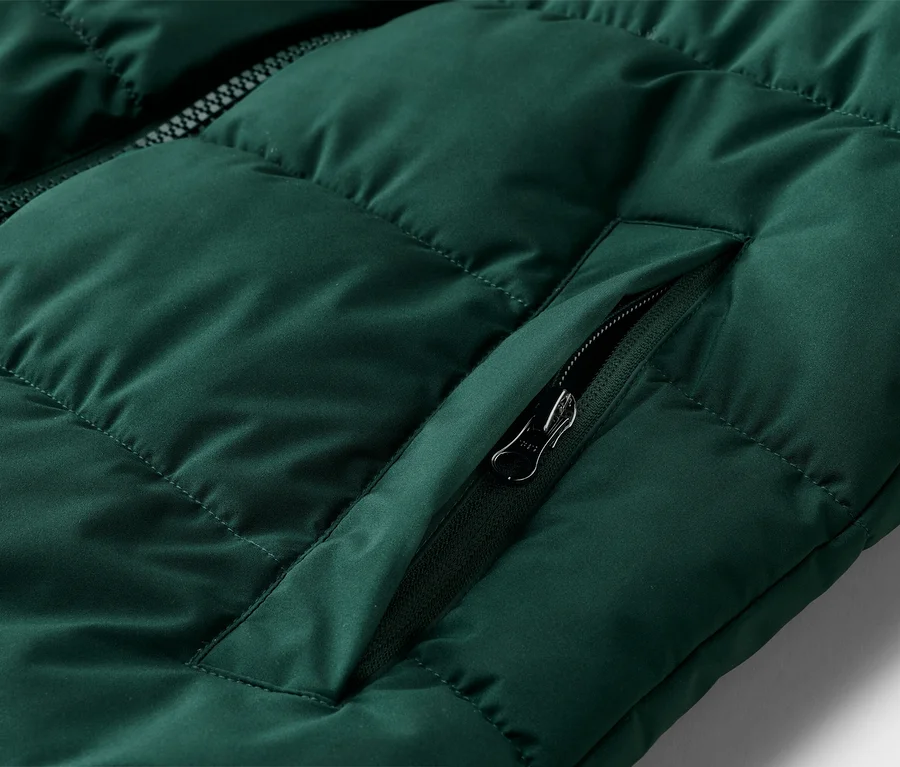 Gros plan d'un gilet matelassé vert émeraude avec fermeture éclair et poche zippée.