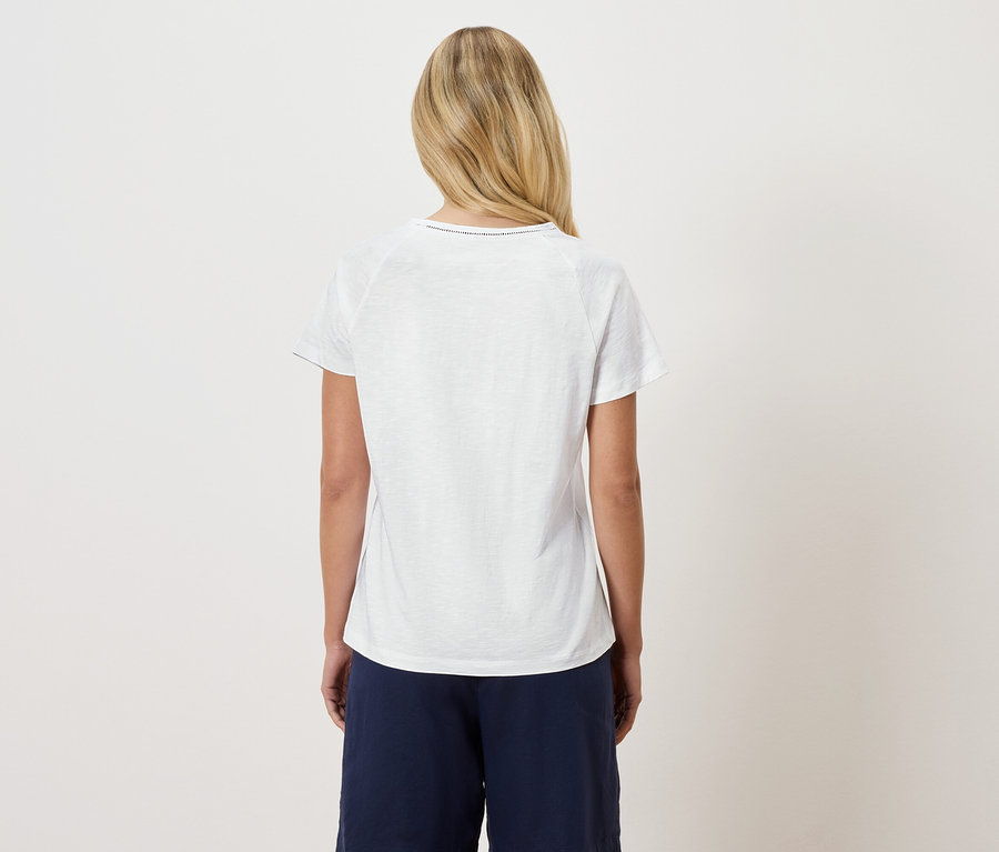 Vue arrière d'une femme blonde portant un t-shirt blanc et un pantalon bleu marine.