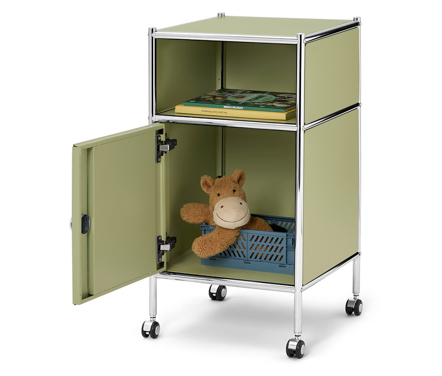 Armoire ouverte vert clair sur roulettes avec un livre dans le compartiment supérieur et une peluche dans une boîte bleue dans le compartiment inférieur.