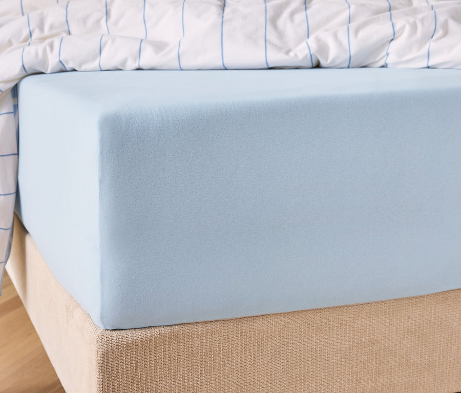 Gros plan d'un drap-housse bleu clair sur un matelas avec une couette à rayures blanches et bleues en arrière-plan.