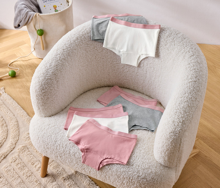 Plusieurs culottes pour filles rose poudré (lot de 7) sont posées sur un fauteuil.