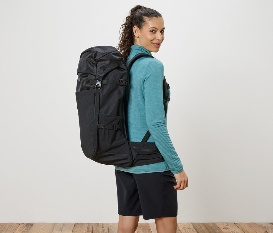 Femme avec un sac à dos noir sur les épaules, regardant par-dessus son épaule.