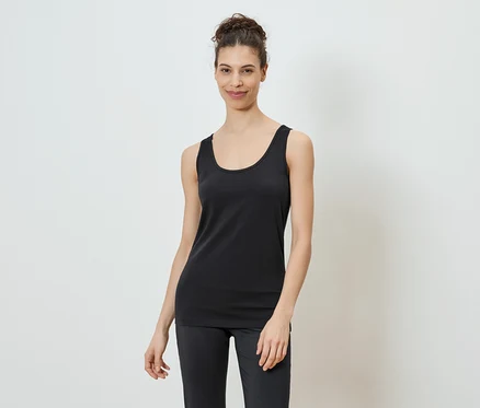 Une femme portant un chignon porte un débardeur noir et un legging sur fond blanc.