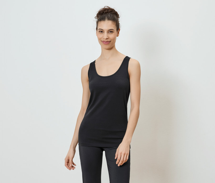 Une femme portant un chignon porte un débardeur noir et un legging sur fond blanc.