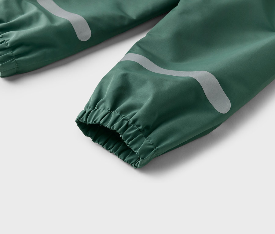 Gros plan d'un pantalon de pluie vert avec des poignets élastiques et des bandes réfléchissantes.