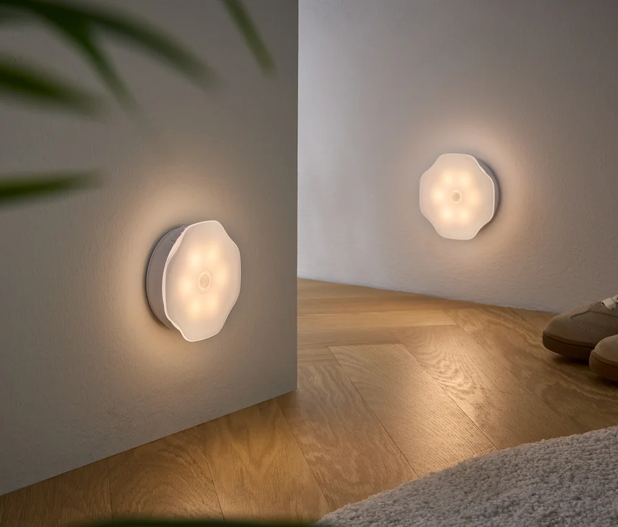 Deux lumières blanches en forme de fleur montées au mur illuminent une pièce avec un plancher en bois et des chaussures beiges.