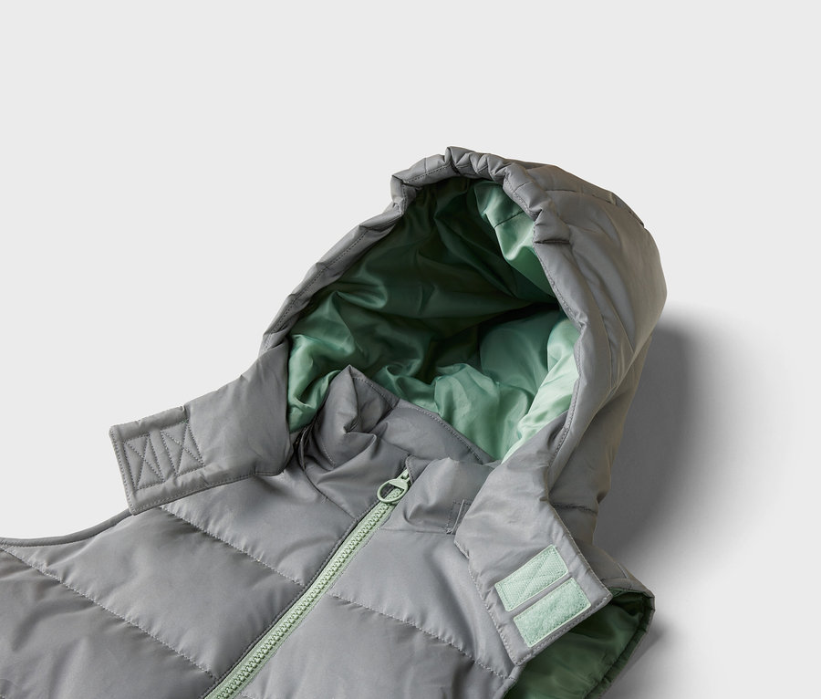 Gros plan d'un gilet matelassé gris avec capuche et doublure vert clair, fermé par une fermeture éclair vert clair.