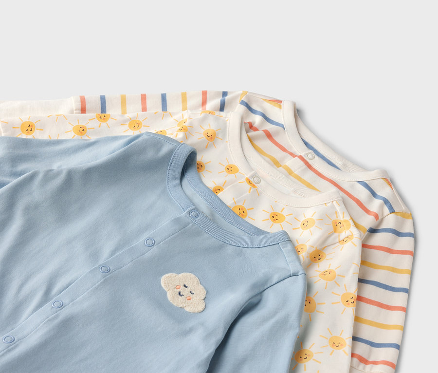 Gros plan sur trois pyjamas pour bébés : bleu clair uni avec un nuage appliqué, blanc avec des soleils et rayé.