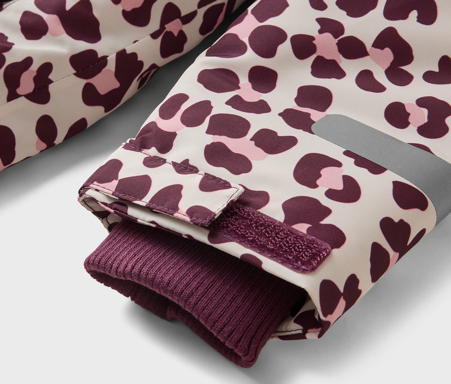 Gros plan d'une manche de veste avec un imprimé léopard beige, violet foncé et rose clair. La manche présente un poignet côtelé violet foncé, une sangle Velcro réglable et une bande réfléchissante.