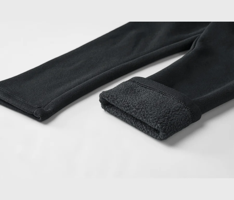 Gros plan d'un pantalon noir, une jambe retroussée pour révéler une doublure en polaire douce et foncée.