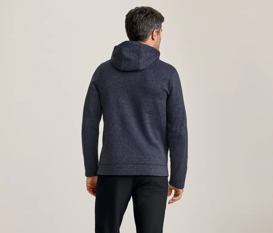 Homme vu de dos, portant un sweat à capuche texturé bleu foncé et un pantalon noir.
