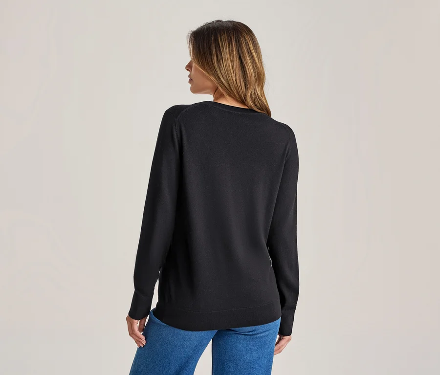 Femme vue de dos, portant un pull noir à manches longues et un jean bleu, la tête légèrement tournée vers la droite.