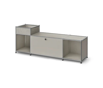Meuble bas modulaire avec cadre métallique et panneaux gris clair. Il comprend un panier perforé sur une étagère ouverte à gauche, un compartiment fermé au centre et une étagère ouverte à droite.