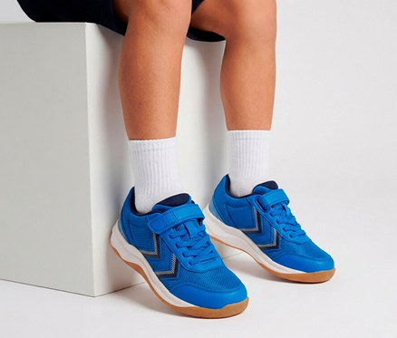 Jambes et pieds d'une personne portant des baskets bleues à scratchs et des chaussettes blanches, assise sur un bloc blanc.