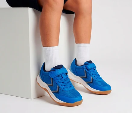 Jambes et pieds d'une personne portant des baskets bleues à scratchs et des chaussettes blanches, assise sur un bloc blanc.