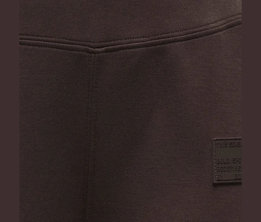 Tissu de vêtement marron foncé avec une couture en V à la taille et une petite étiquette sombre à droite.