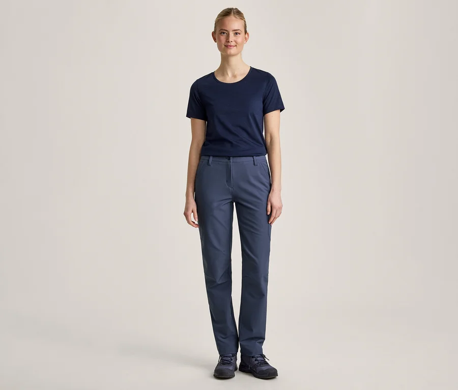 Une jeune femme se tient de face devant un fond clair, vêtue d'un t-shirt bleu marine, d'un pantalon bleu et de chaussures bleu foncé.