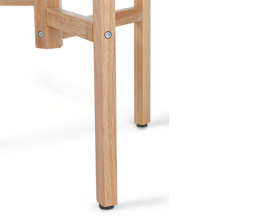 Détail du pied d'une chaise ou d'un tabouret en bois clair avec un pied noir.