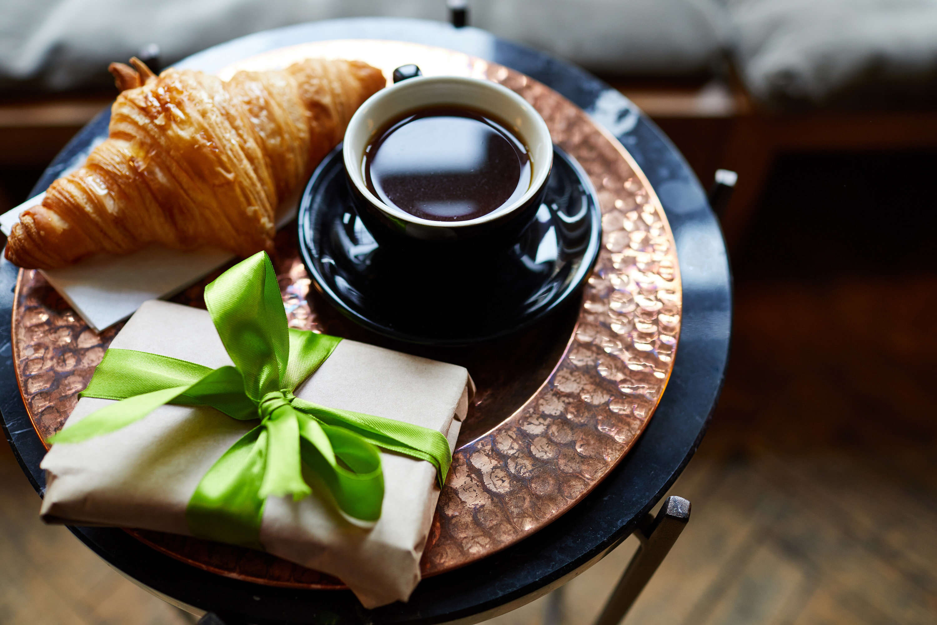 Sur une table, un croissant, une tasse de café et un cadeau emballé avec un ruban vert.
