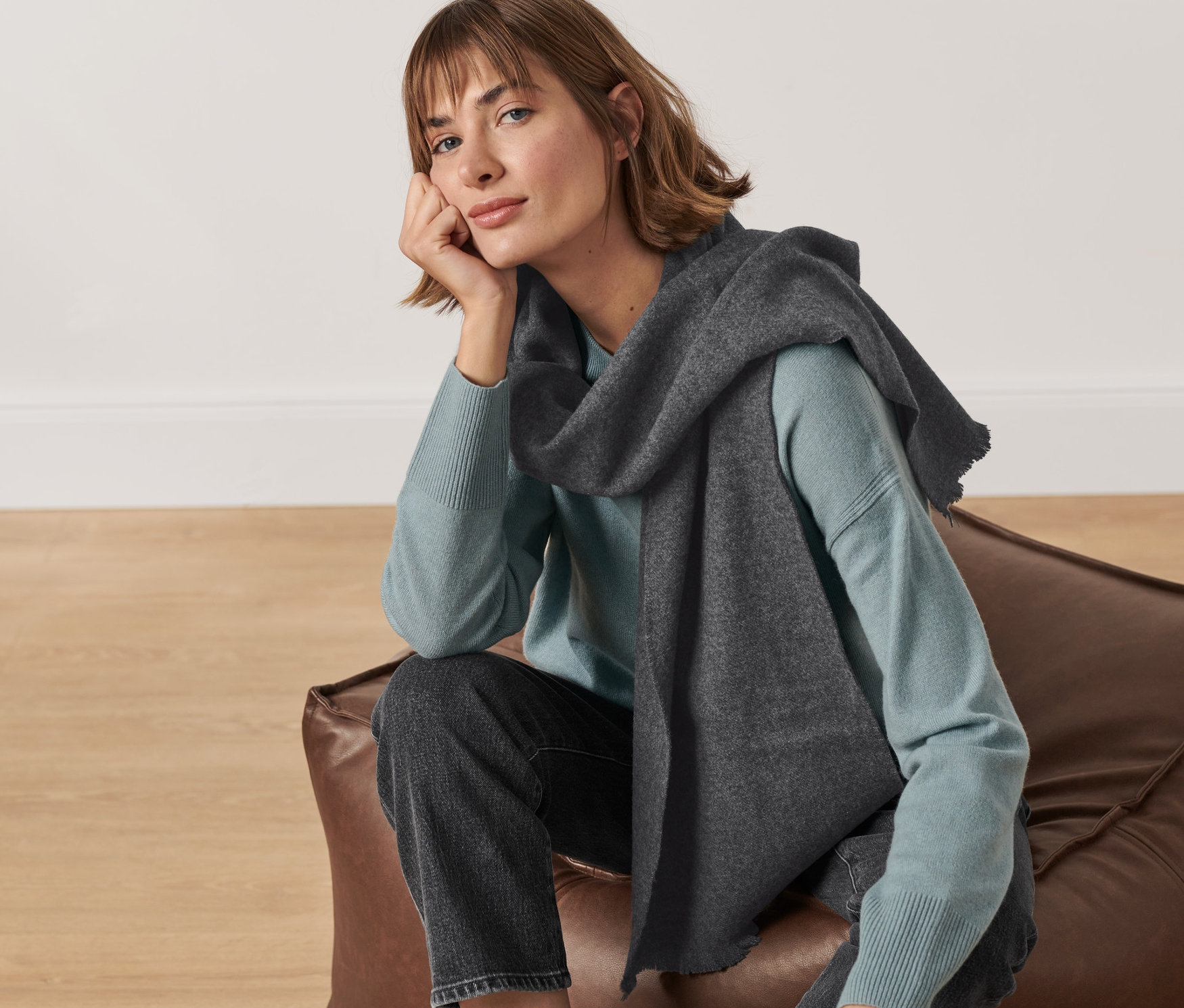 Une femme est assise sur un pouf en cuir et porte une écharpe en cachemire.