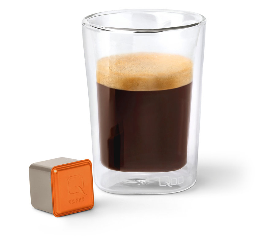 Un verre de Qbo Caffè MINAS VERDE à côté d'une capsule.