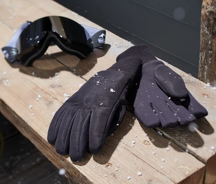 Des gants en maille noirs et des lunettes de ski reposent sur un banc en bois.