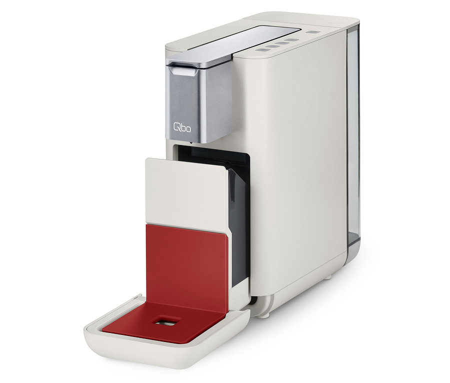 Une machine à café Qbo ESSENTIAL Bright Coral avec un compartiment à capsules ouvert.