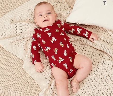 Bébé allongé dans 2 bodys pour bébé sur une couverture en tricot beige à côté d'un coussin blanc avec un visage d'ours.
