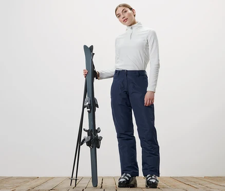 Femme tenant des skis et portant un pantalon de ski.