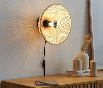 Une lampe murale avec abat-jour en bambou est accrochée au mur au-dessus d'une commode en bois.