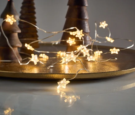 Micro-guirlande lumineuse à LED, étoiles, posée sur un plateau doré à côté de sapins décoratifs en bois.