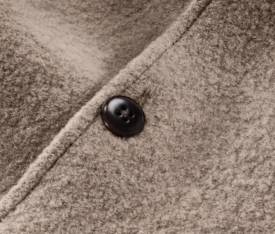 Gros plan sur une combinaison marron pour bébé en laine mérinos avec un bouton.