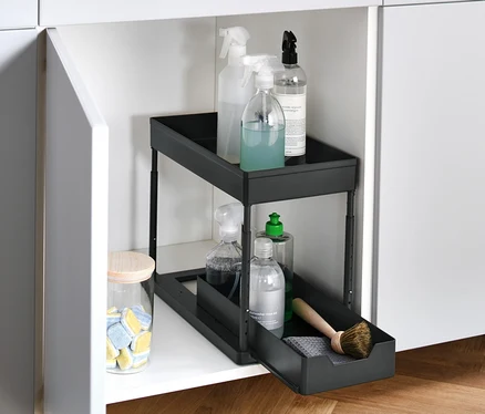 Un placard blanc ouvert avec un élément d’armoire réglable en hauteur contenant des produits de nettoyage.