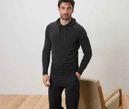 Un homme pose, portant un pull à capuche en maille fine.