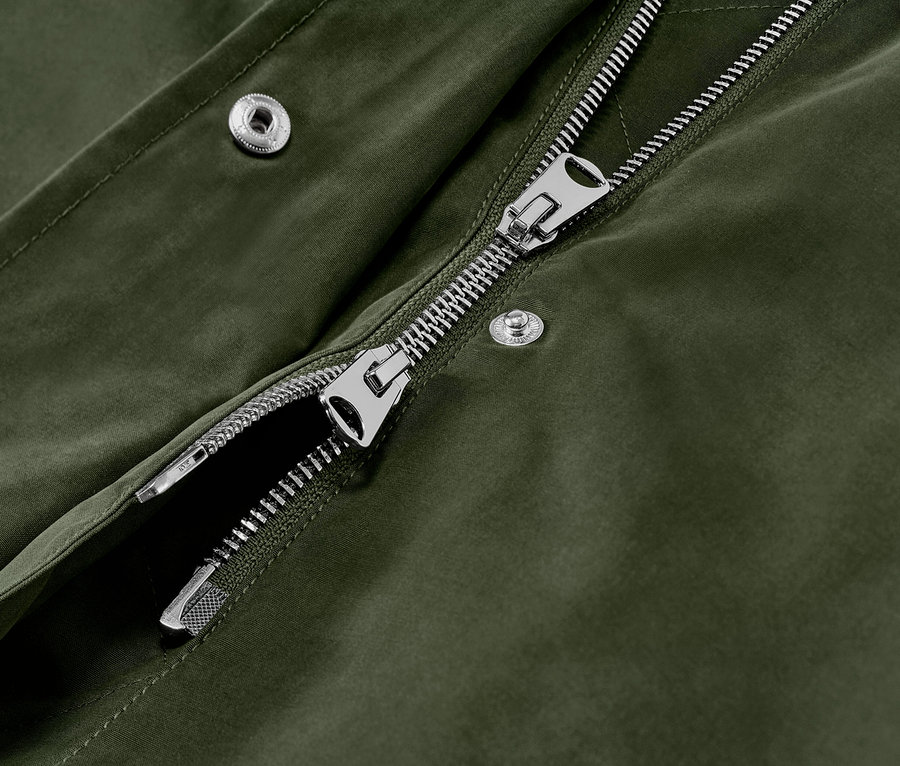 Détail d'une parka à capuche verte avec fermeture éclair argentée et boutons-pression.