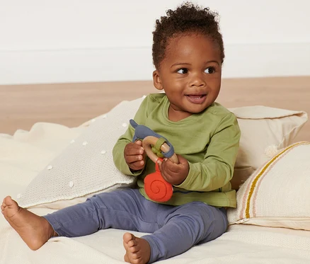 Un bébé souriant est assis sur une couverture et tient un jouet de préhension.