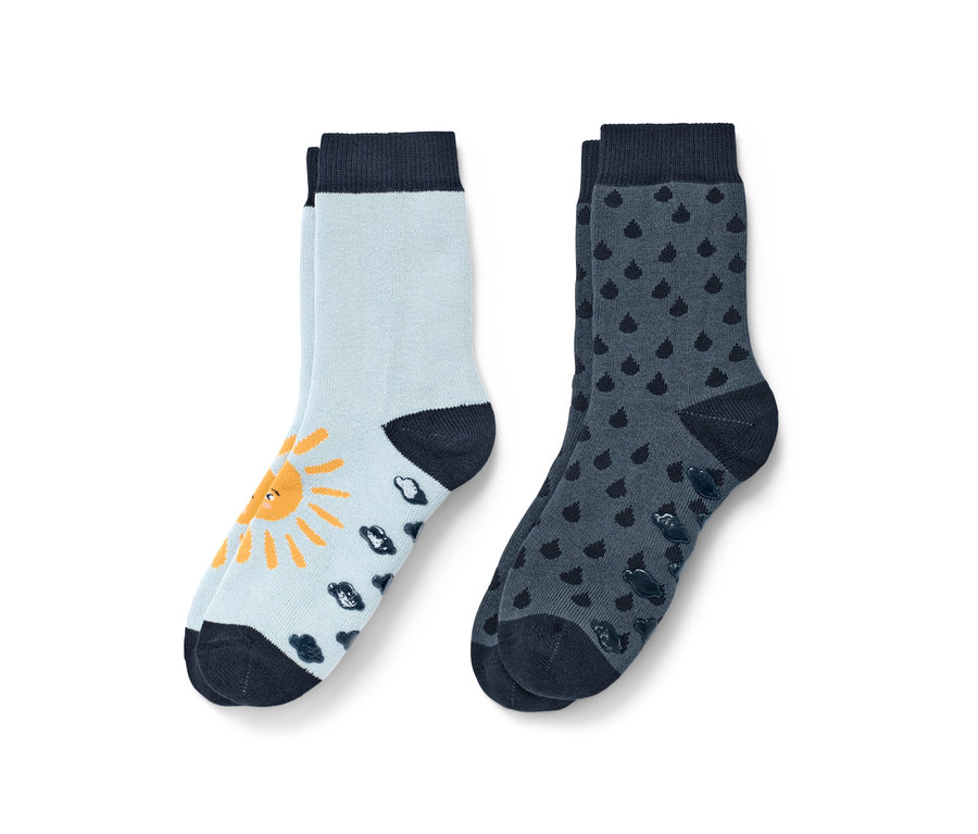 Deux paires de chaussettes antidérapantes bleues pour tout-petit. Une paire bleu clair avec un soleil jaune et des nuages bleu foncé, l'autre bleu foncé avec des gouttes.