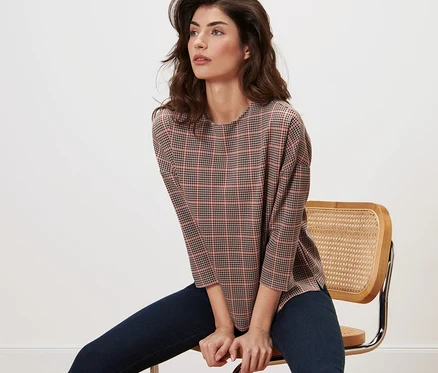 Femme assise sur une chaise portant un sweat-shirt manches 3/4, pied de poule.