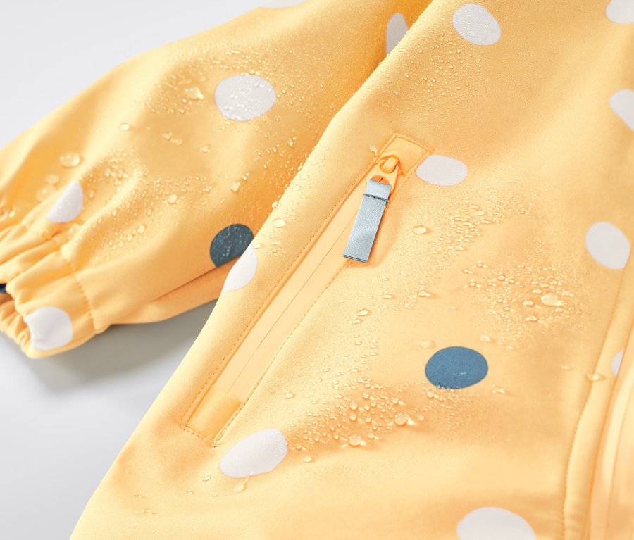 Détail d'une combinaison softshell pour enfant avec un imprimé intégral à pois.