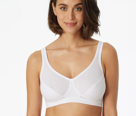 Une femme porte une brassière SCHIESSER blanche à bonnets et regarde l'appareil photo.