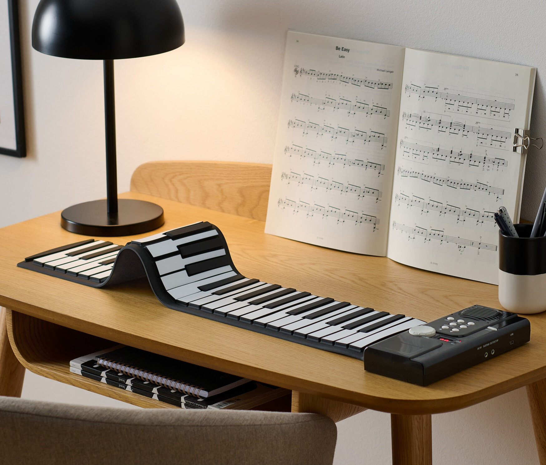 Sur une table se trouvent un piano électronique enroulable, des partitions et une lampe.