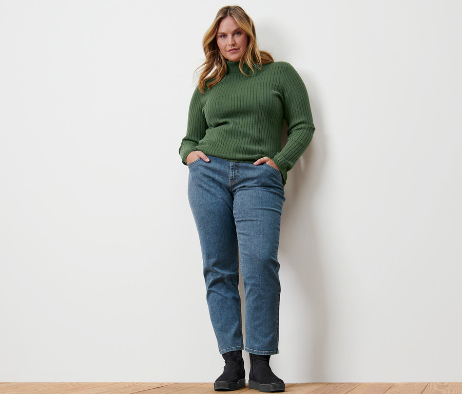Femme posant, portant un pull à col roulé côtelé vert.