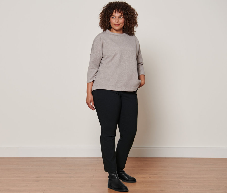 Femme posant dans un sweat-shirt beige à manches 3/4, des bottines en cuir noires et un pantalon noir prêt à porter en bengaline.