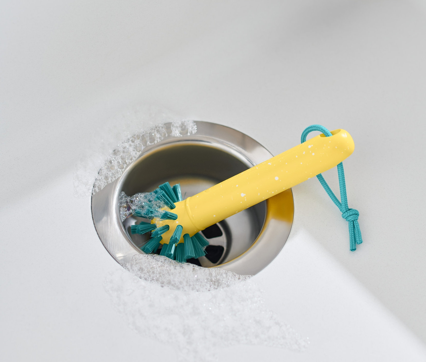 Brosse de nettoyage universelle jaune dans un évier en acier inoxydable avec de la mousse et une serviette beige.