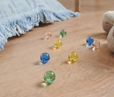 Des billes lumineuses de différentes couleurs sont posées sur le sol à côté d'un chien en peluche et d'une couverture bleue.