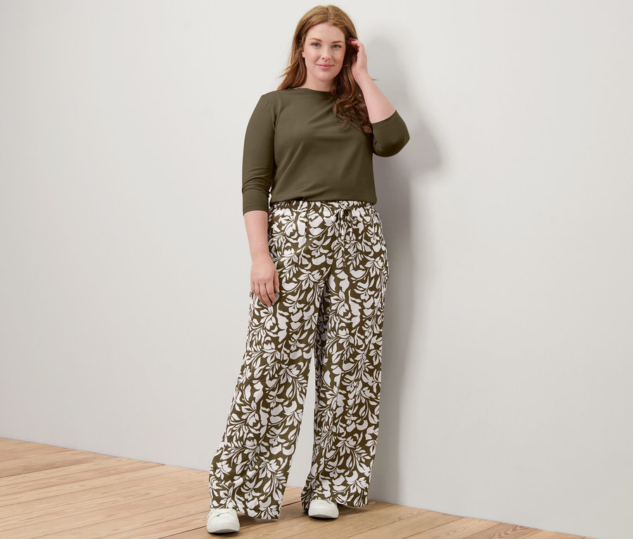 Une femme pose, portant un t-shirt kaki à manches 3/4 et un pantalon imprimé à taille élastique.